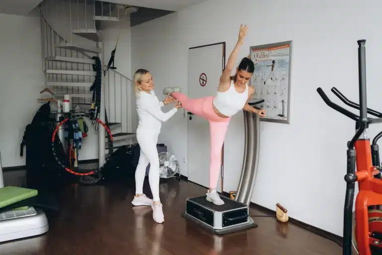 Trainer hilft Frau beim Dehnen auf Vibrationsplatte mit VacuStep zur Hautbildverbesserung im Fitnessstudio Düsseldorf.