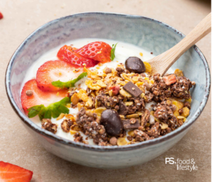 Schale mit Joghurt, darauf Granola, Schokolade und Erdbeeren als Dessert angerichtet.