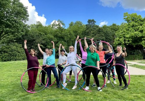 Frauen stehen im Freien mit Hula-Hoop-Reifen und tauschen Fitness-Tipps für die Sommerfigur aus.