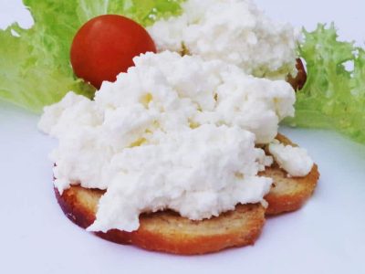 Geröstete Brotscheiben mit Hüttenkäse, Kopfsalat und einer Kirschtomate auf einem Teller serviert.