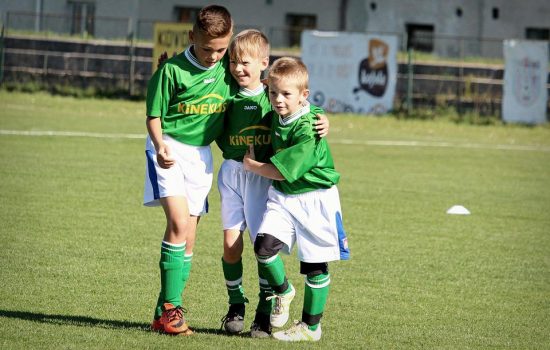 Drei Jungen in grünen Fußballtrikots umarmen und freuen sich auf einen Präventionskurs für Grundschulkinder.