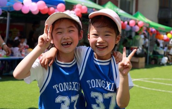 Zwei Kinder in blauen Trikots zeigen beim Präventionskurs für Grundschüler das Peace-Zeichen und spielen mit Luftballons.
