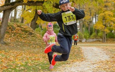 Junge springt beim Präventionskurs für Grundschulkinder auf herbstlichem Waldweg während eines Rennens.