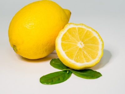 Ganze und halbierte Zitronen liegen auf grünen Blättern, Thema: Lebensmittel zur Entgiftung und Reinigung des Körpers.