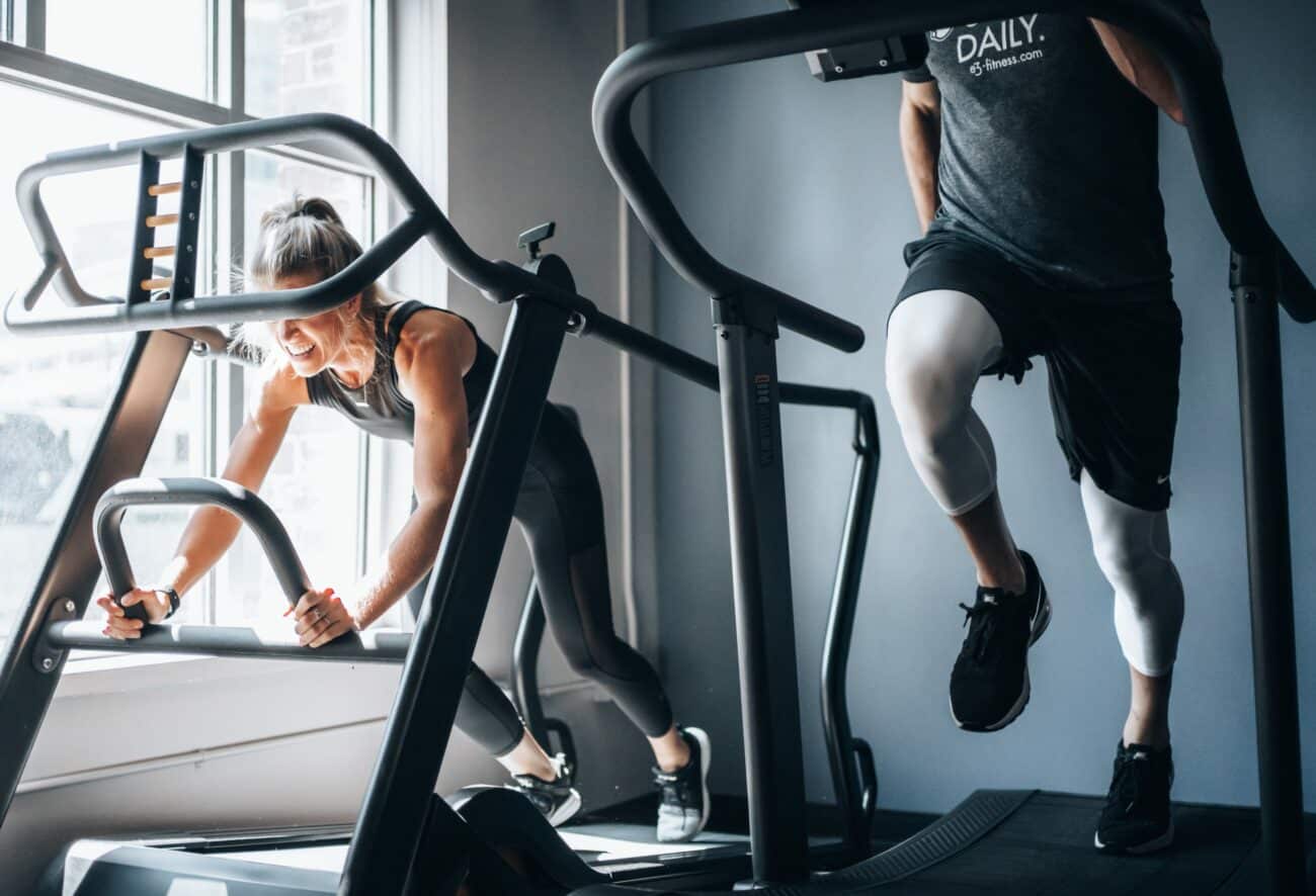 Zwei Personen laufen im Fitnessstudio nebeneinander auf Laufbändern.