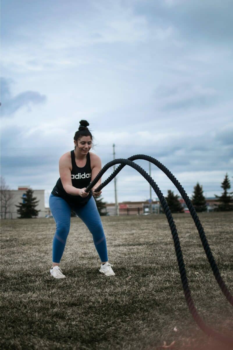 Frau in Sportkleidung trainiert draußen mit Battle Ropes.
